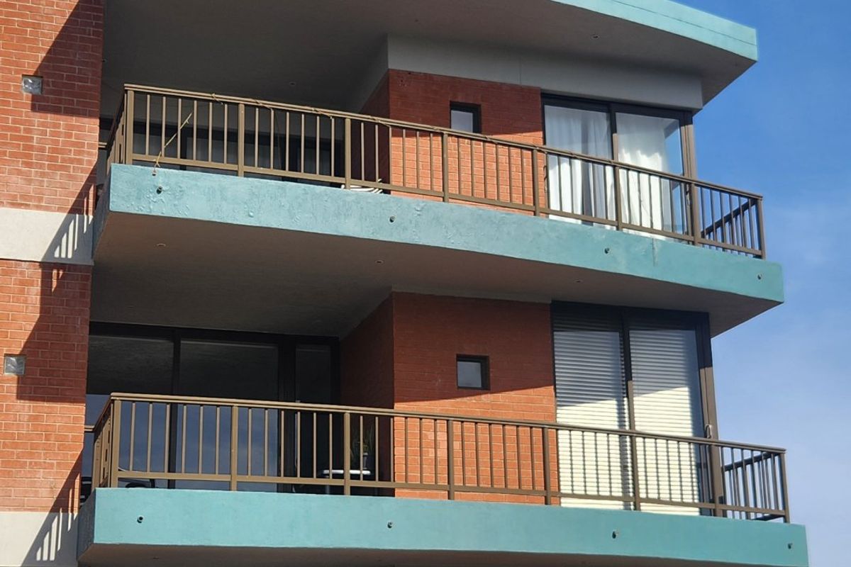 Exterior view of a multi-story apartment building featuring brick facade, private balconies with metal railings, and sliding glass doors.