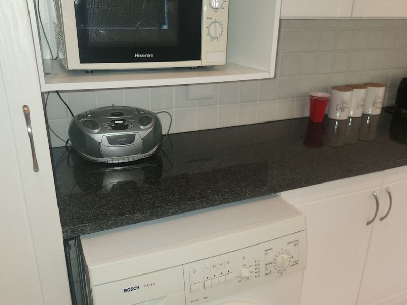 A functional laundry area featuring built-in cabinetry, a dark granite countertop, tiled backsplash, and an integrated washing machine.