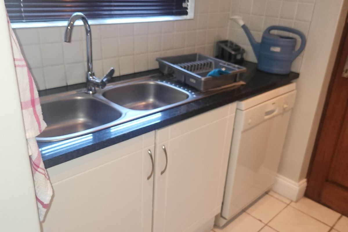 A functional kitchen area featuring a double bowl stainless steel sink, white cabinetry, tiled splashback, and tiled flooring.