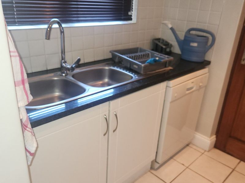 A functional kitchen area featuring a double bowl stainless steel sink, white cabinetry, tiled splashback, and tiled flooring.
