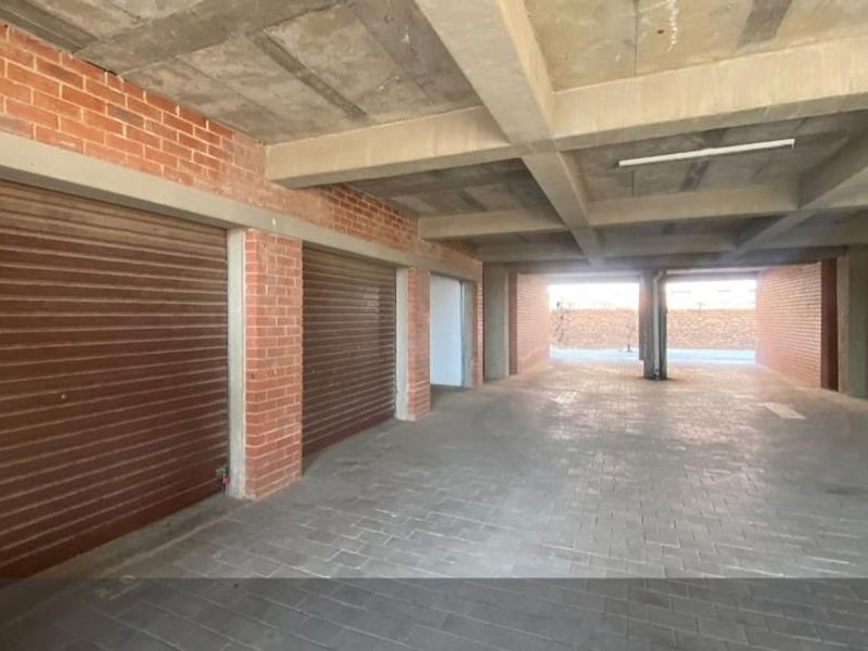 A spacious, open-plan communal garage area featuring exposed concrete ceilings, brick wall construction, and durable paved flooring with multiple roller shutter doors.