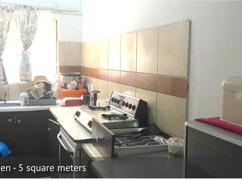 Compact kitchen featuring a stainless steel sink, tiled splashback, and a freestanding stove with laminate countertops and built-in cabinetry.