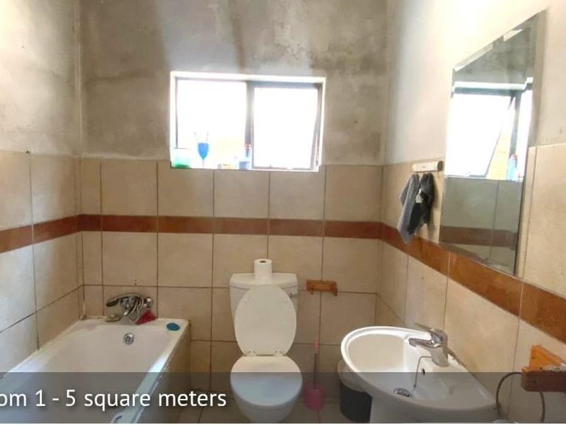 A compact bathroom featuring a bathtub, pedestal basin, and toilet, currently requiring finishing work on the upper wall surfaces.