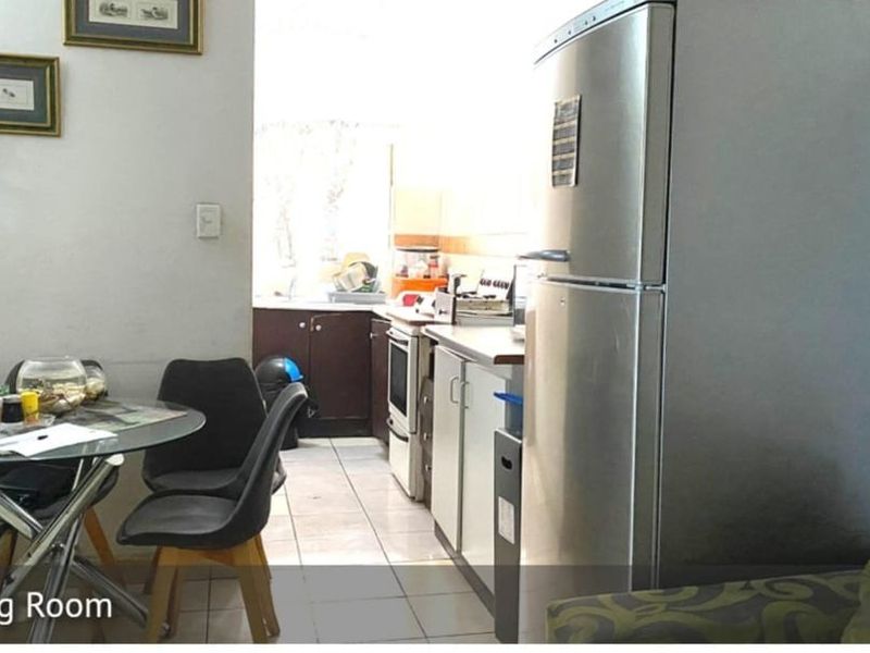 An open-plan dining area adjacent to a functional kitchen featuring tiled floors, built-in cabinetry, and a standard oven setup.