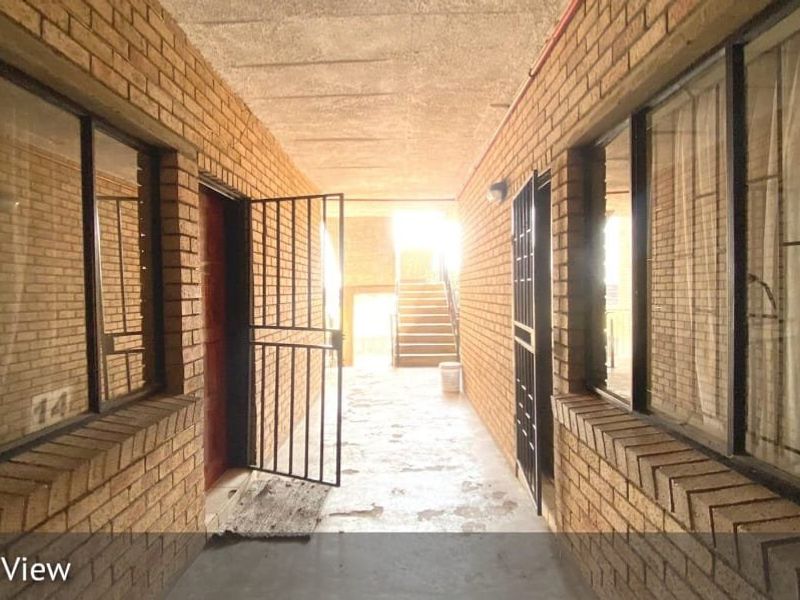 An exterior-facing hallway featuring brick walls, security gates, and a concrete ceiling leading to a staircase.