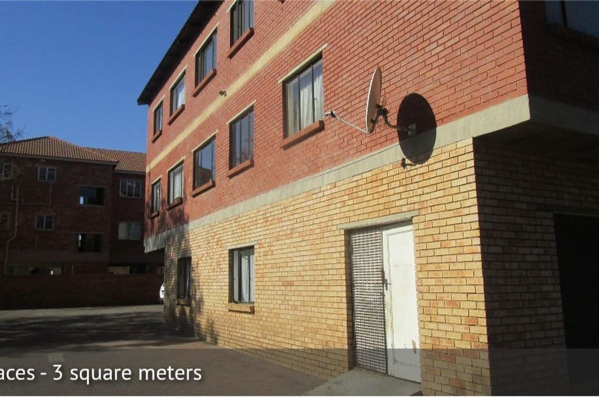 Exterior view of a multi-story townhouse complex featuring face brick construction, paved driveway access, and security gate entrance.