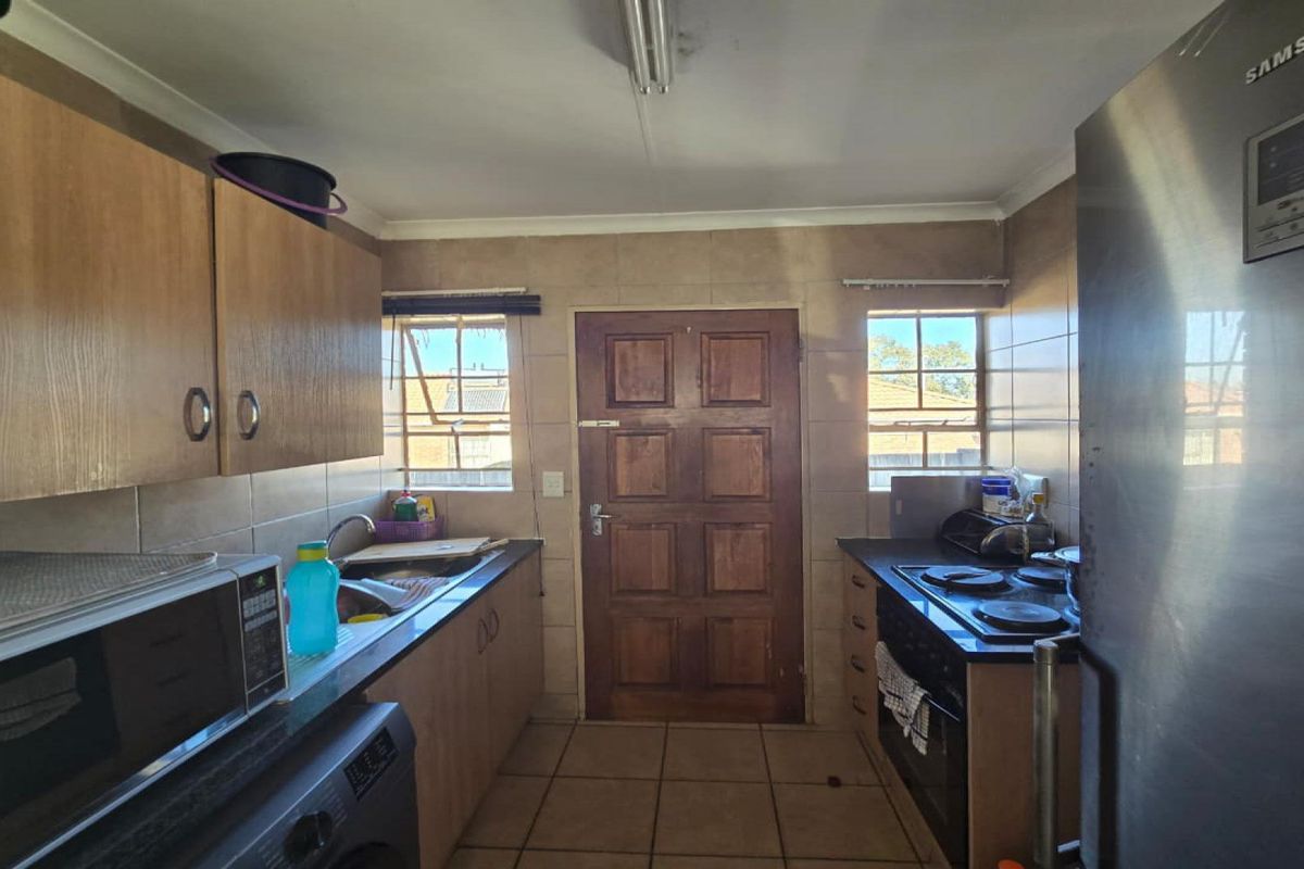 Functional kitchen featuring built-in cabinetry, laminate countertops, electric hob, oven, and tiled finishes with direct access to the exterior.