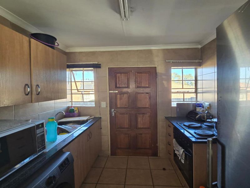 Functional kitchen featuring built-in cabinetry, laminate countertops, electric hob, oven, and tiled finishes with direct access to the exterior.