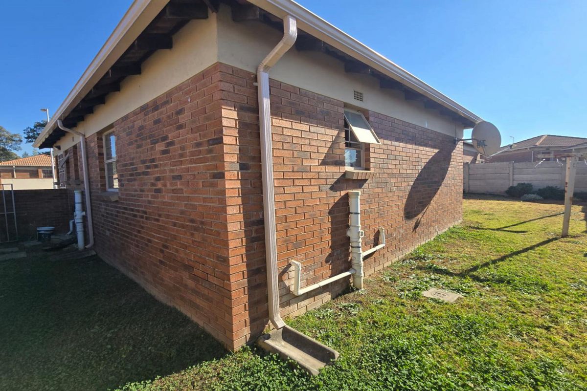 A view of the rear exterior of the house featuring face brick walls, exposed eaves, and external plumbing fixtures set within a grassed yard.