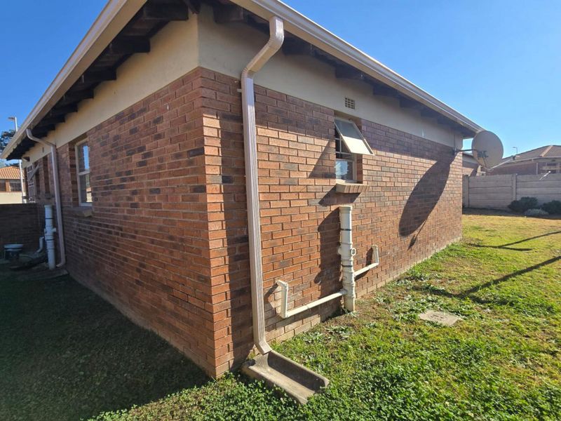 A view of the rear exterior of the house featuring face brick walls, exposed eaves, and external plumbing fixtures set within a grassed yard.