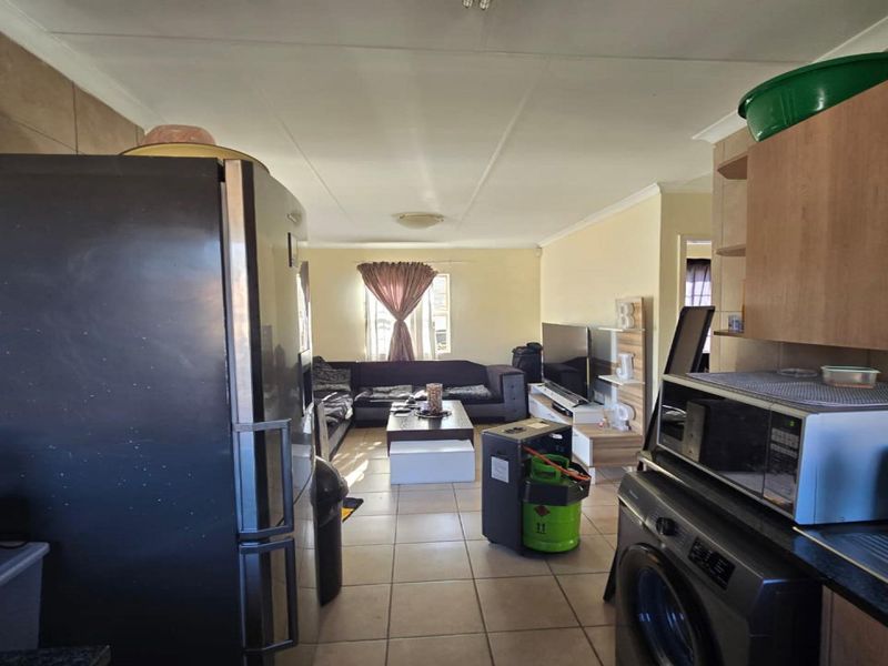 Open-plan living area featuring a functional kitchen space with built-in cabinetry and tiled flooring, flowing into a comfortable lounge area.