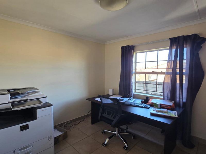 A functional home office space featuring tiled flooring, a window with security bars, and a built-in cupboard for storage.