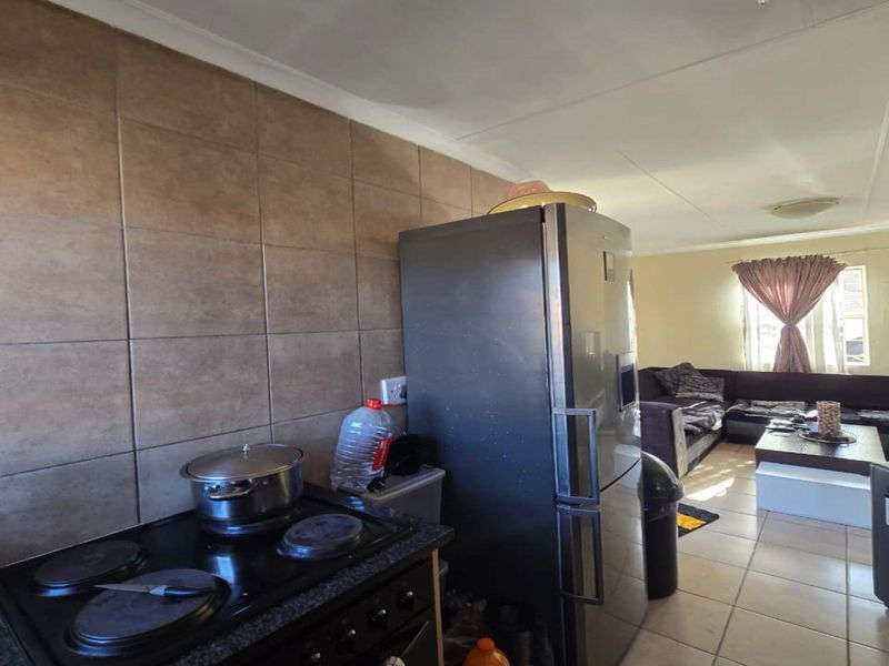 Open plan living area featuring a kitchen corner with tiled splashback and built-in stove, flowing into a combined lounge space with tiled flooring.