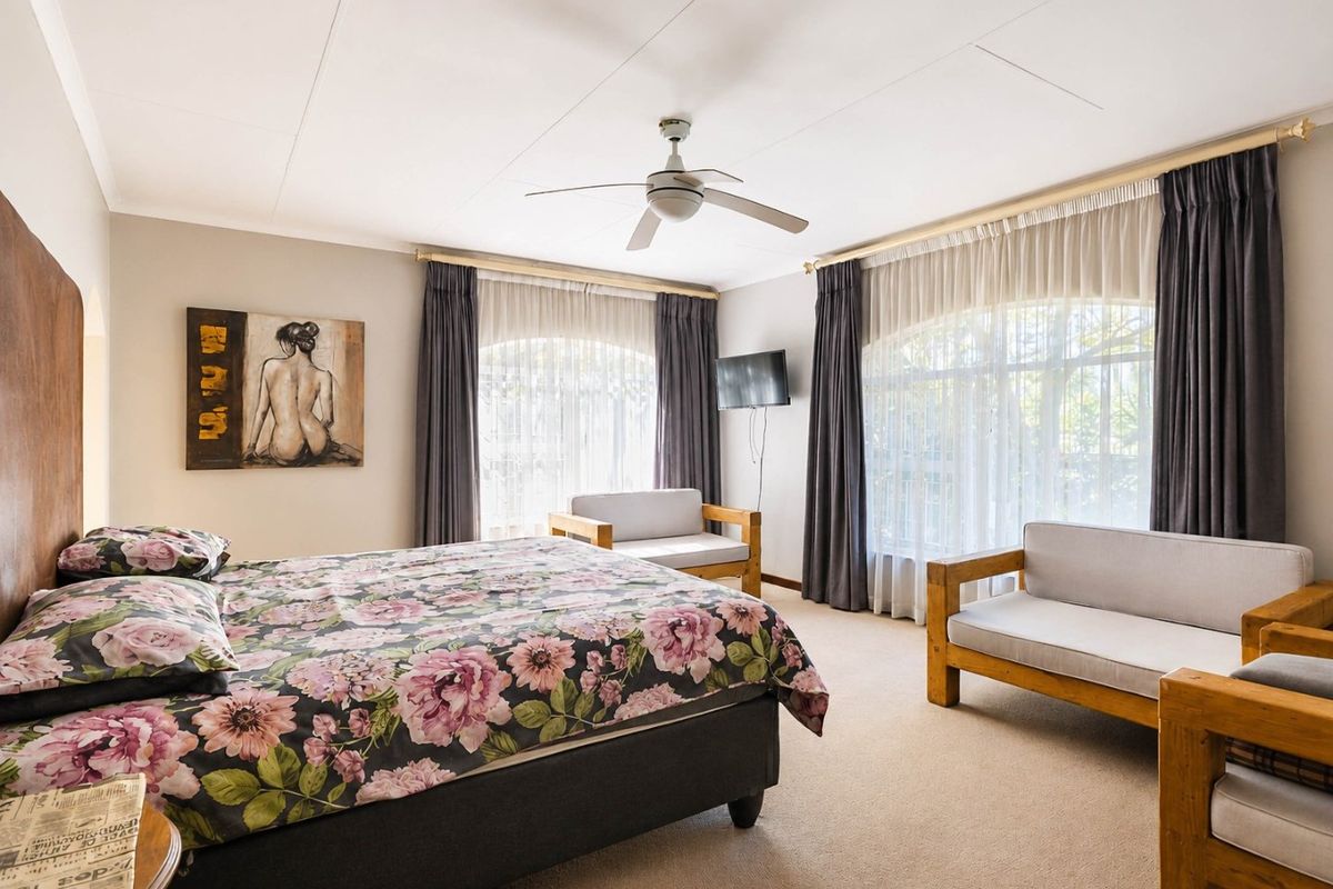 Spacious bedroom featuring neutral wall tones, carpeted flooring, and a ceiling fan, with large windows providing ample natural light.