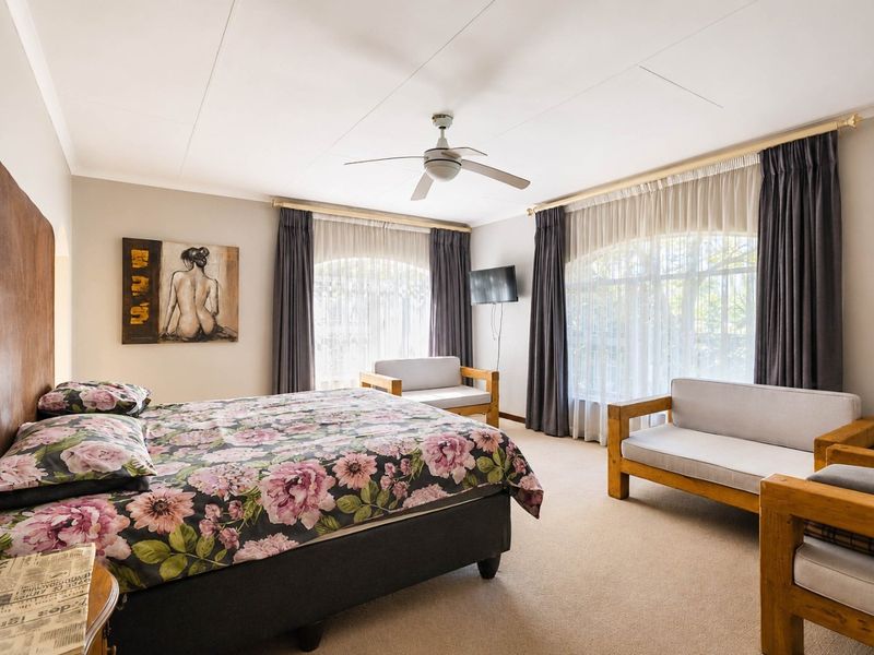 Spacious bedroom featuring neutral wall tones, carpeted flooring, and a ceiling fan, with large windows providing ample natural light.