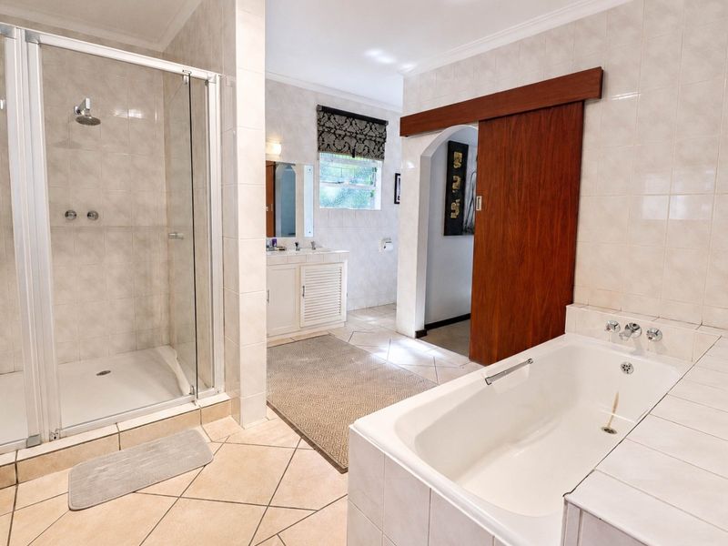 Spacious bathroom featuring a glass-enclosed shower, built-in bathtub, vanity cabinet, and neutral wall and floor tiling with a sliding wooden door.