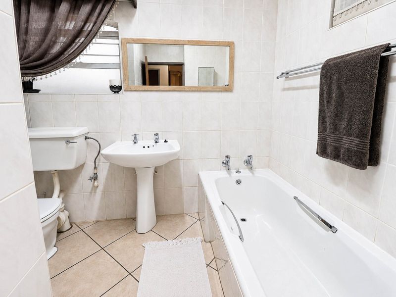 A functional bathroom featuring a pedestal basin, standard toilet, and a bathtub with tiled walls and flooring.