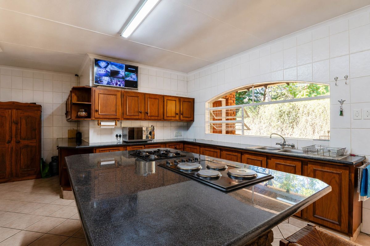 Spacious kitchen featuring dark granite countertops, extensive wooden cabinetry, dual hobs, and a large window overlooking the garden.