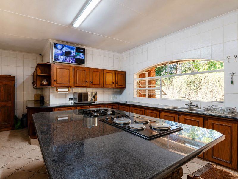 Spacious kitchen featuring dark granite countertops, extensive wooden cabinetry, dual hobs, and a large window overlooking the garden.