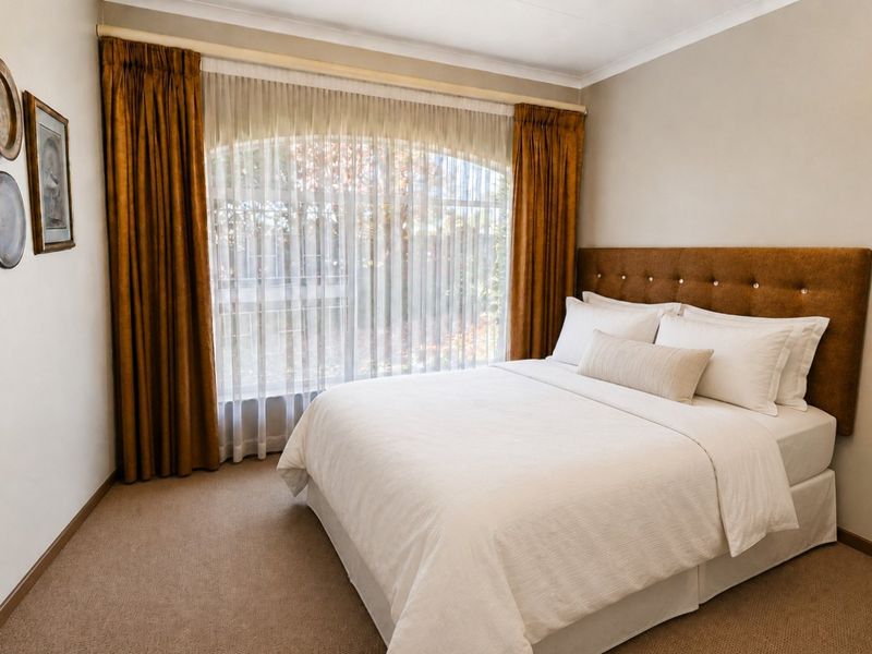 A well-maintained bedroom featuring neutral carpeting, an arched window with layered curtains, and a clean, neutral interior finish.