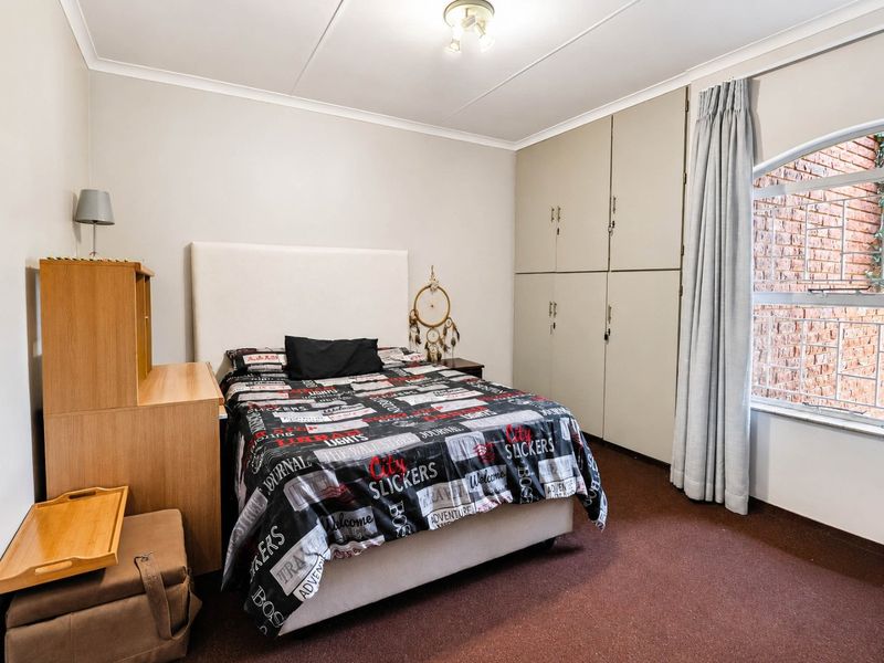 A functional bedroom featuring built-in cupboards, carpeted flooring, and a window with security bars, offering a neutral base for personalization.