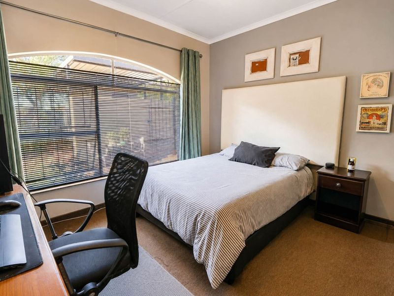 A well-maintained bedroom featuring a large arched window with venetian blinds and neutral wall tones.