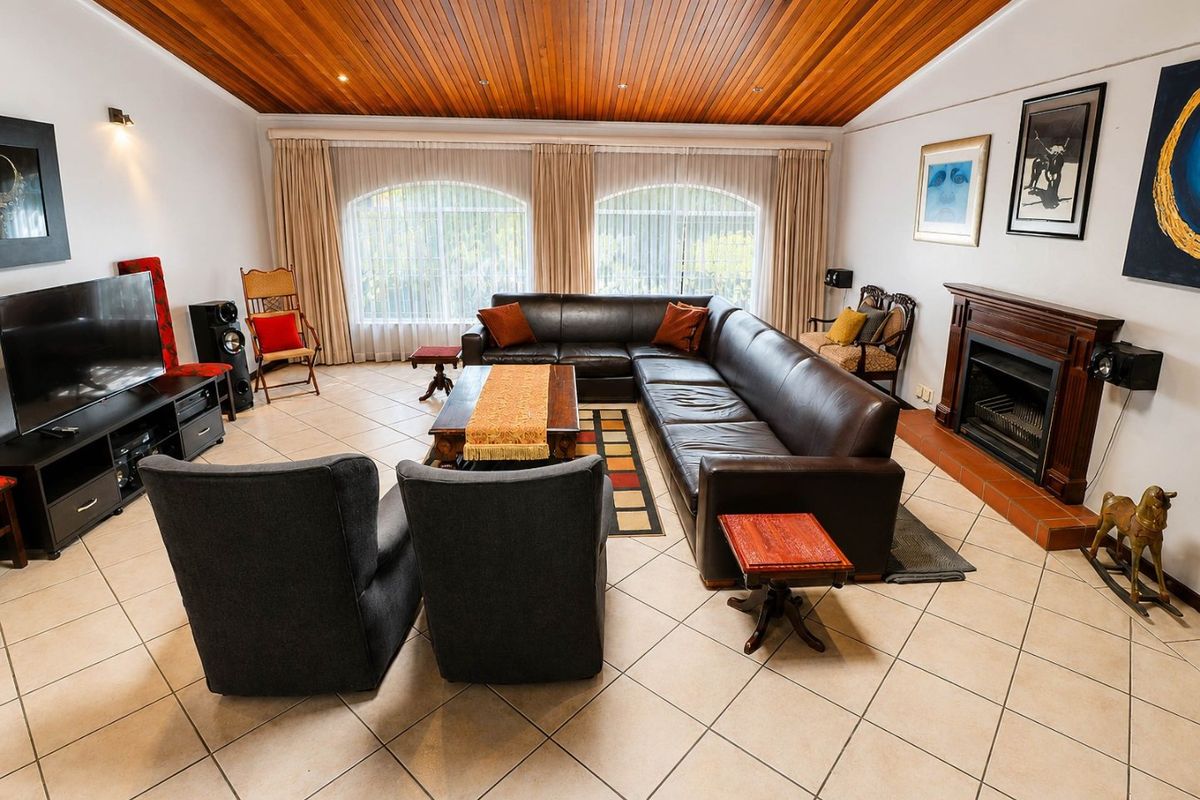 Spacious living room featuring a warm timber-paneled ceiling, tiled flooring, and a classic built-in fireplace with a timber mantel.