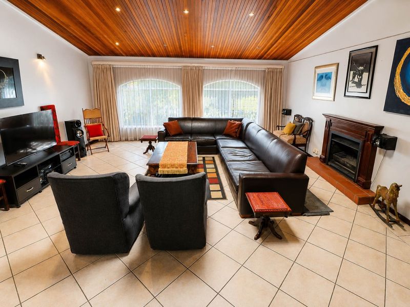 Spacious living room featuring a warm timber-paneled ceiling, tiled flooring, and a classic built-in fireplace with a timber mantel.