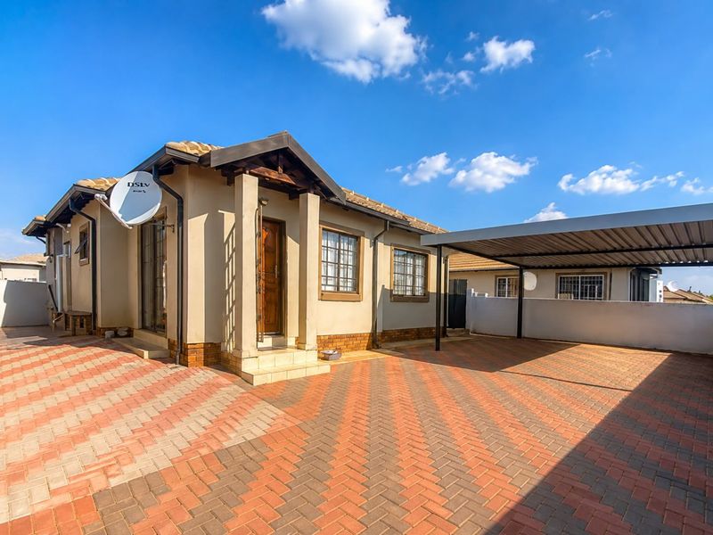 Front exterior view of a townhouse featuring a paved driveway, a covered carport, and a tiled roof with security bars on the windows.