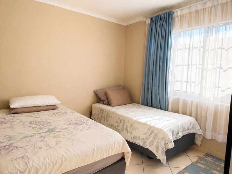A functional bedroom featuring tiled flooring and large windows with installed curtain rails, providing natural light and a neutral base for interior design.