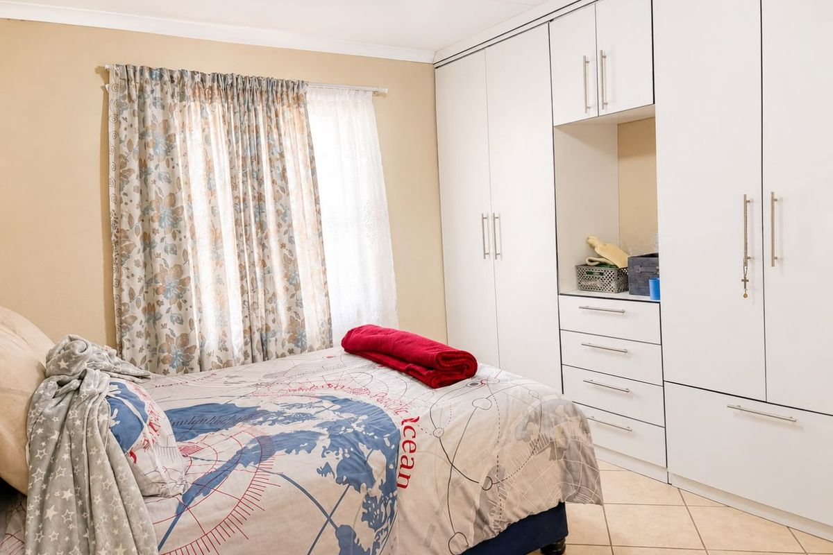 A well-maintained bedroom featuring extensive white built-in cupboards with integrated drawers and neutral tiled flooring.