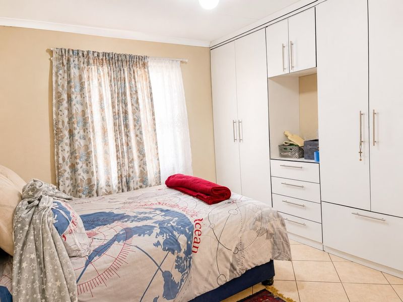 A well-maintained bedroom featuring extensive white built-in cupboards with integrated drawers and neutral tiled flooring.