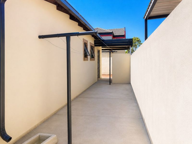 A clean and well-maintained side utility area featuring concrete paving, a fixed washing line, and a protective awning.
