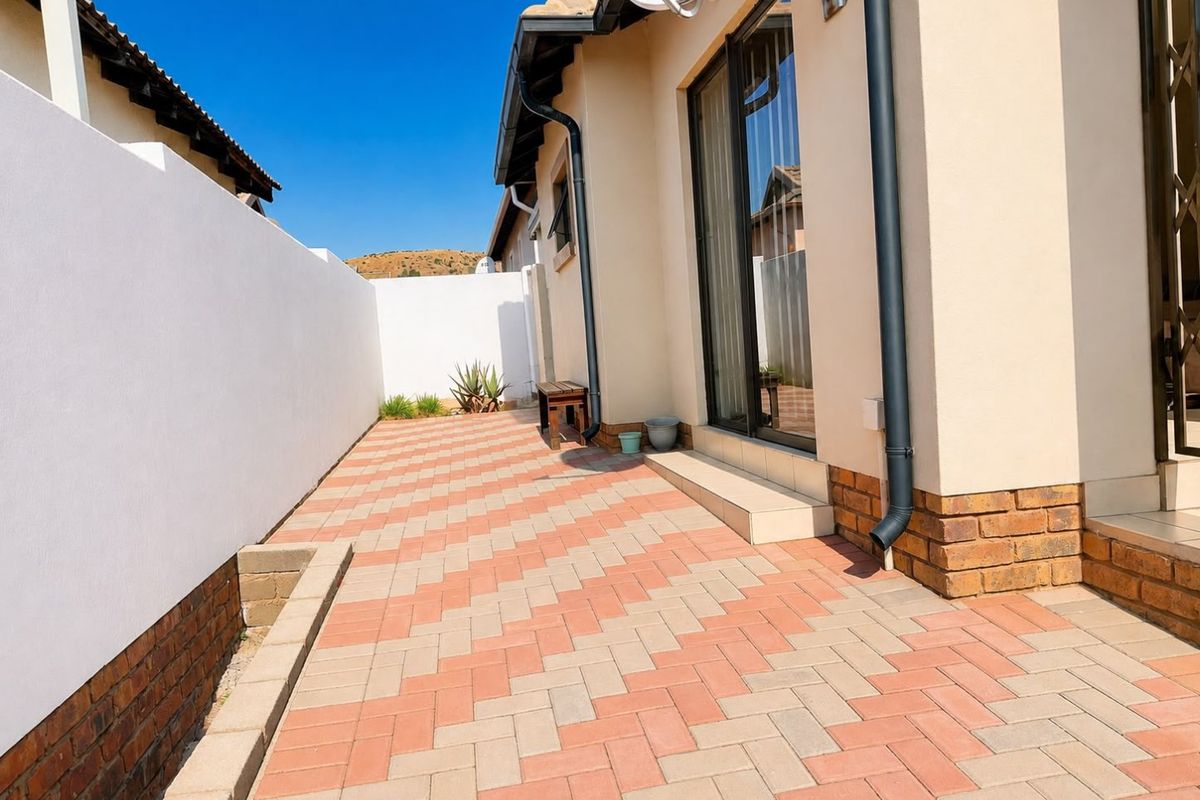A clean, paved rear patio area featuring a brick boundary wall and sliding glass door access to the townhouse interior.