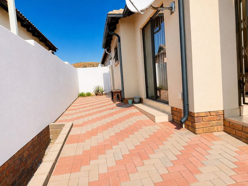 A clean, paved rear patio area featuring a brick boundary wall and sliding glass door access to the townhouse interior.