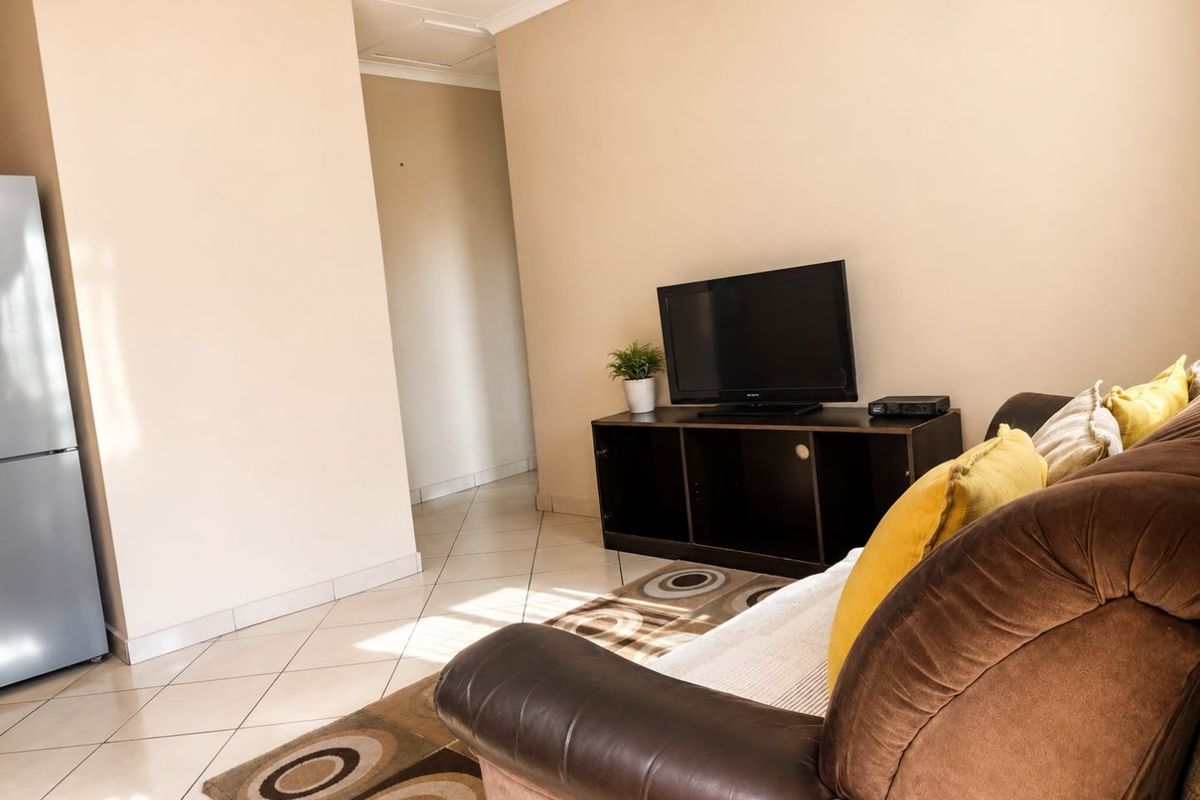 A living room area featuring neutral wall tones and tiled flooring, providing a functional space with access to an adjoining hallway.