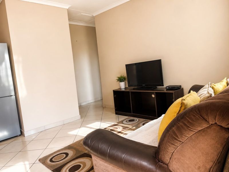 A living room area featuring neutral wall tones and tiled flooring, providing a functional space with access to an adjoining hallway.