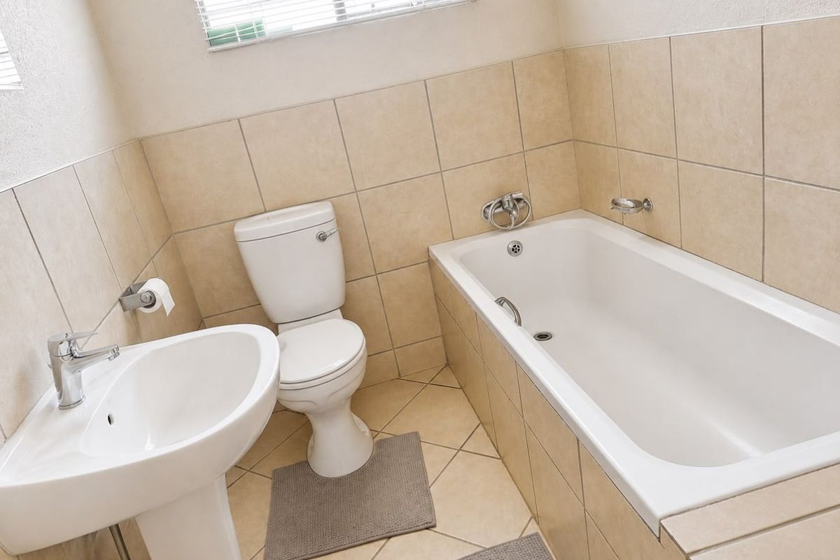A functional bathroom featuring a pedestal basin, toilet, and bathtub with neutral wall and floor tiling.