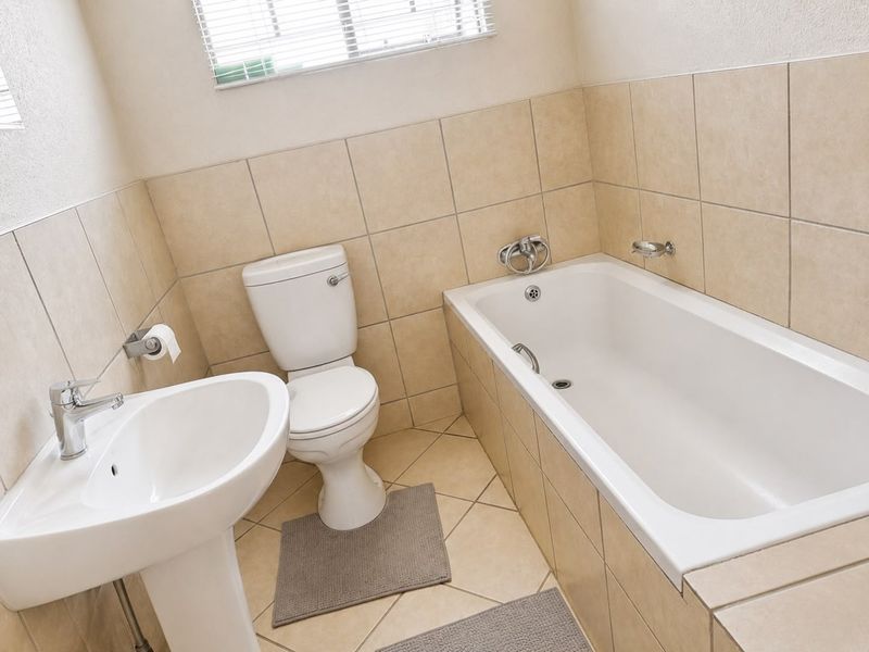 A functional bathroom featuring a pedestal basin, toilet, and bathtub with neutral wall and floor tiling.