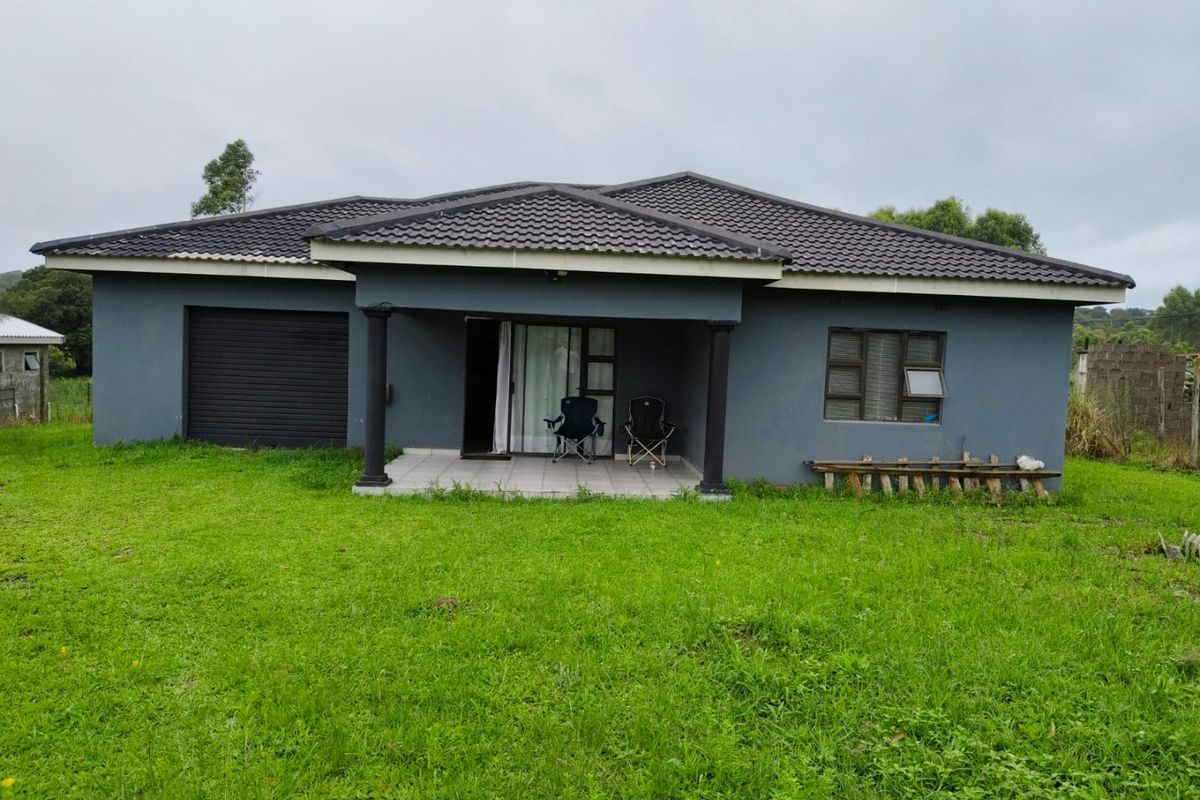 Rear view of a single-story house featuring a covered patio, tiled roof, and attached garage, set on a large grassed plot.