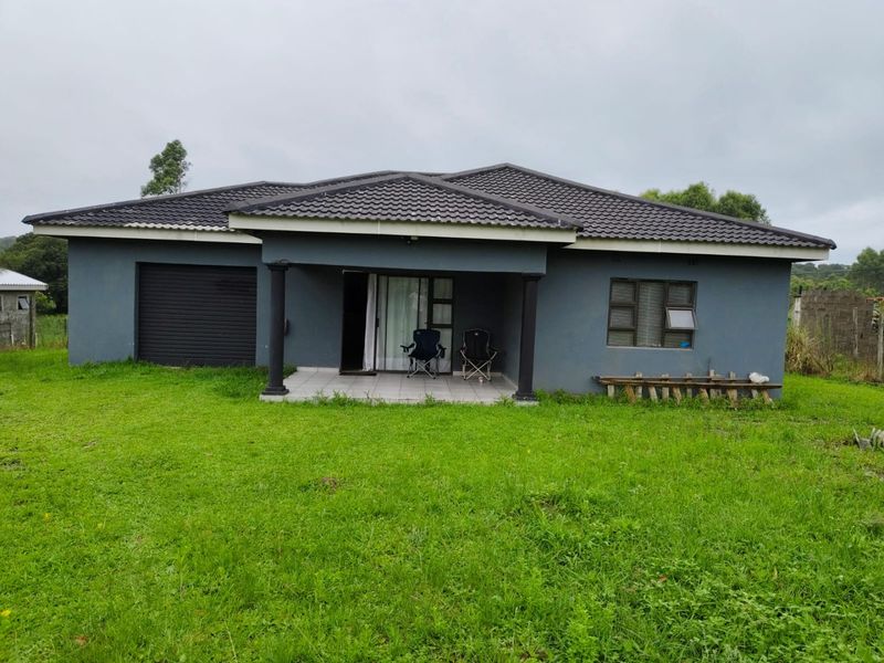 Rear view of a single-story house featuring a covered patio, tiled roof, and attached garage, set on a large grassed plot.