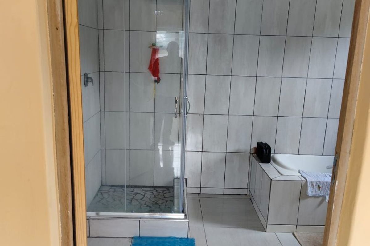 A functional bathroom featuring a glass shower enclosure, a built-in bathtub, and full-height wall tiling.