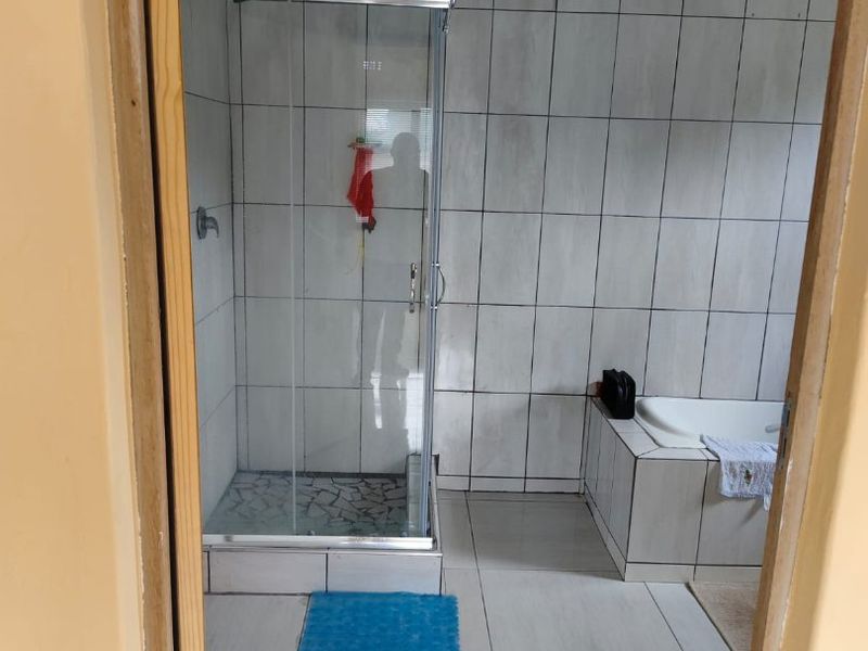 A functional bathroom featuring a glass shower enclosure, a built-in bathtub, and full-height wall tiling.