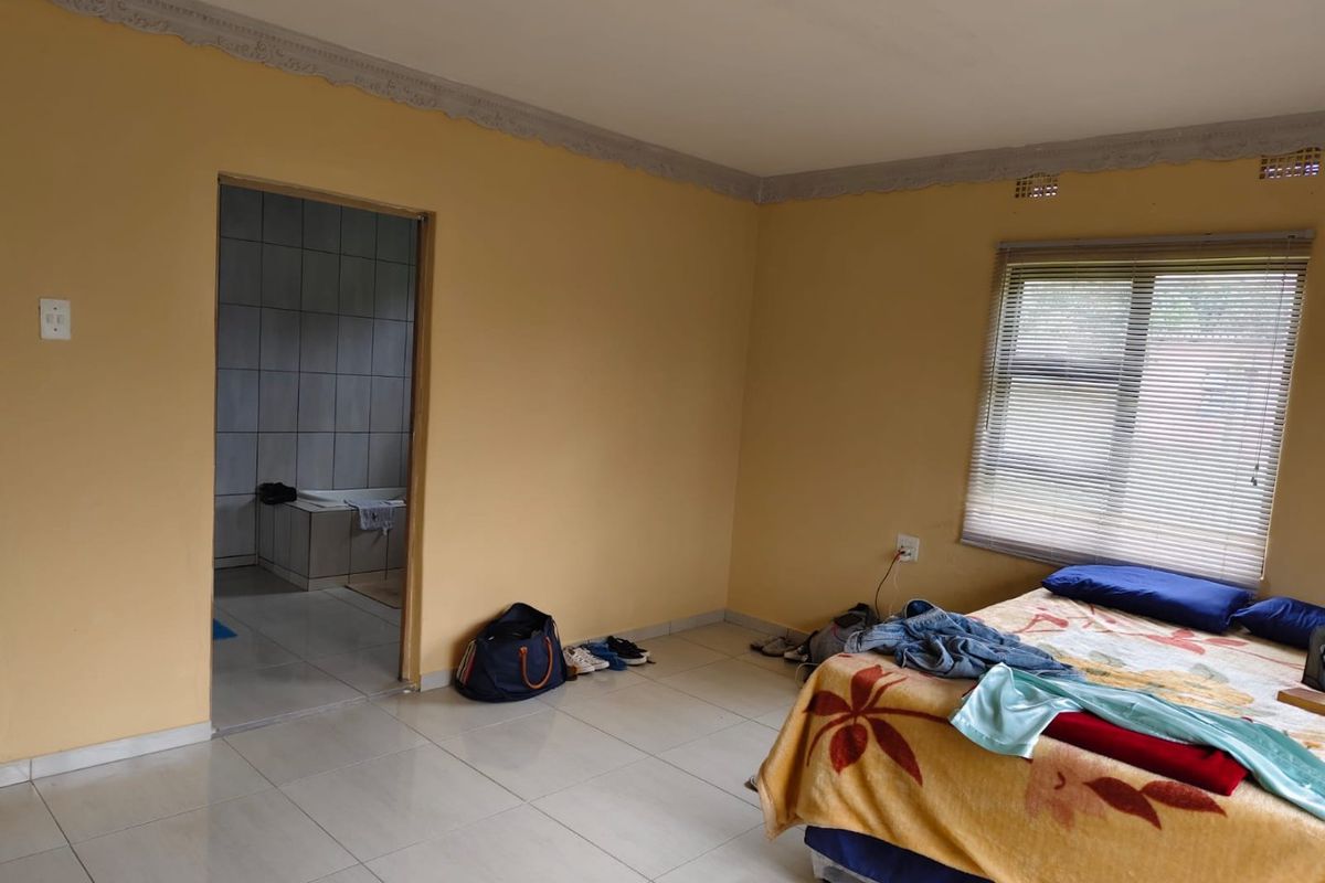 A bedroom featuring tiled flooring, decorative ceiling cornices, and an adjoining en-suite bathroom with tiled walls.