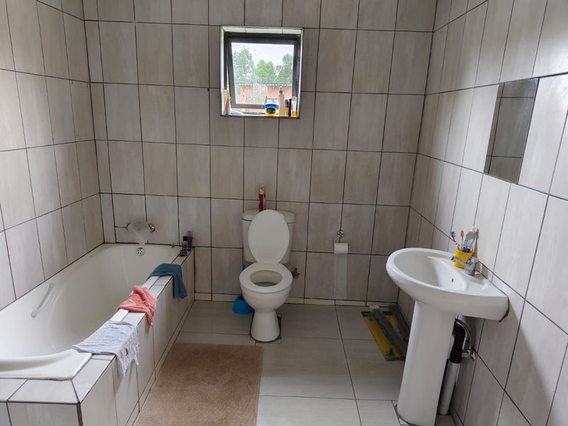 A functional bathroom featuring a bathtub, pedestal sink, and toilet with full-height wall tiling and a small window for natural light.