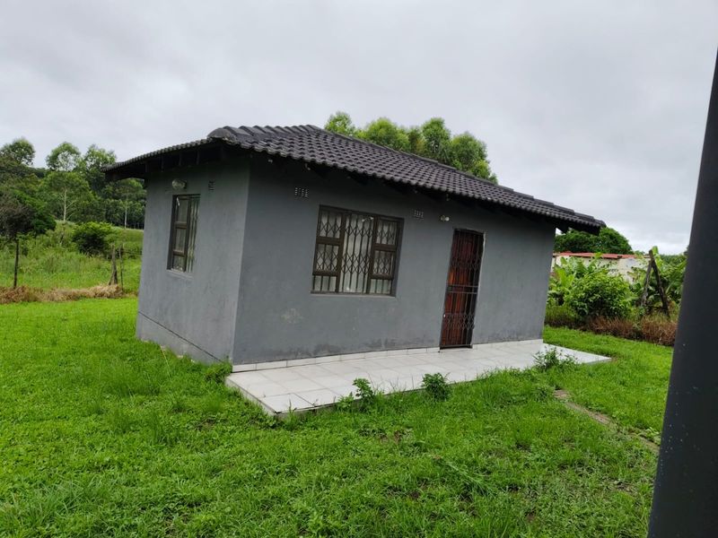 A detached outbuilding featuring a tiled roof, security bars on windows, and a small tiled patio area set within a grassy yard.