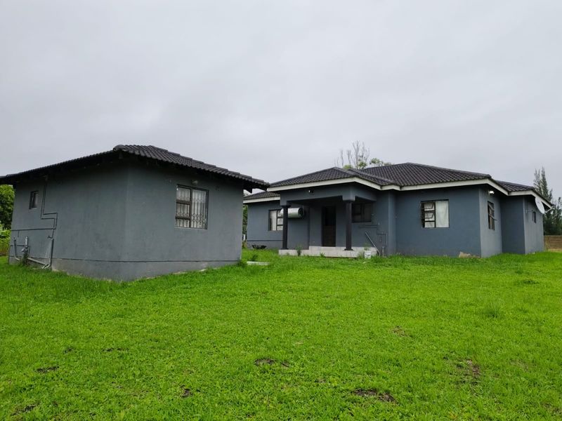 Rear view of a detached house featuring a grey painted exterior, tiled roof, and a small covered porch area set within a large lawn.