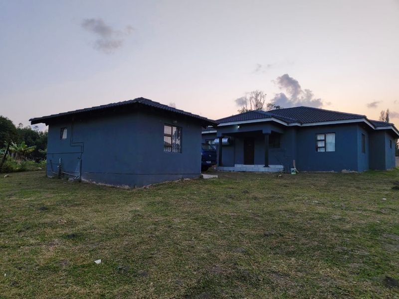 A view of the rear exterior of the house featuring a dark blue painted facade, tiled roof, and aluminium window frames set on a large plot.