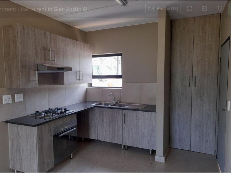 Modern kitchen featuring light wood-grain cabinetry, dark countertops, a gas hob, built-in oven, extractor fan, and a tall pantry cupboard.