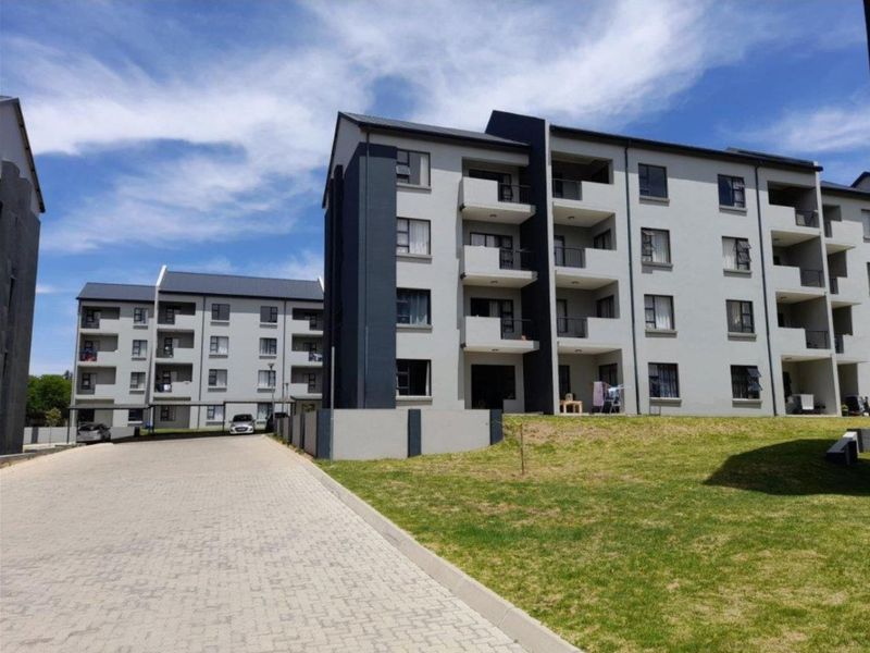 A modern multi-story apartment complex featuring a paved driveway, landscaped lawn, and private balconies on each level.
